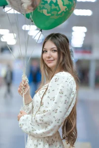 Девушка с воздушными шариками улыбается на быстрой фотосессии на природе.